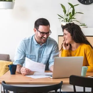 Smiling couple managing finances, reviewing their bank accounts using laptop computer and calculator at modern kitchen